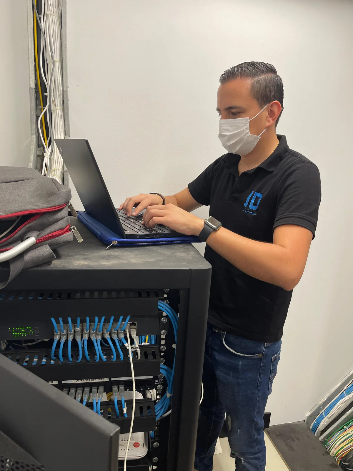 Técnico de JD SPECIALIST trabajando con un computador junto a un rack de comunicaciones.